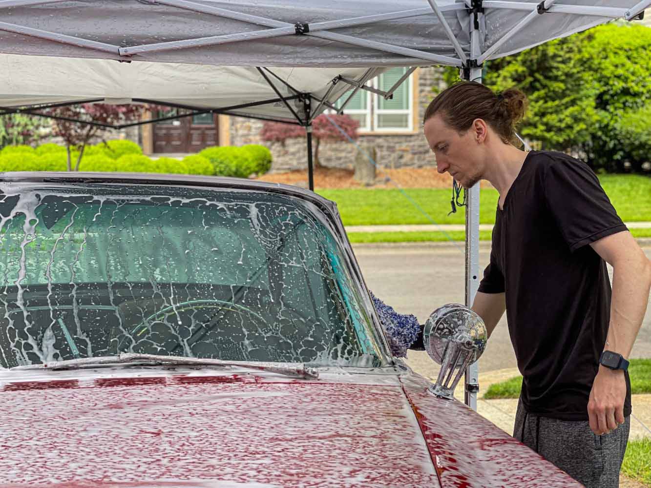 Auto detailer washing 1961 Chrysler 300G in driveway under tarp